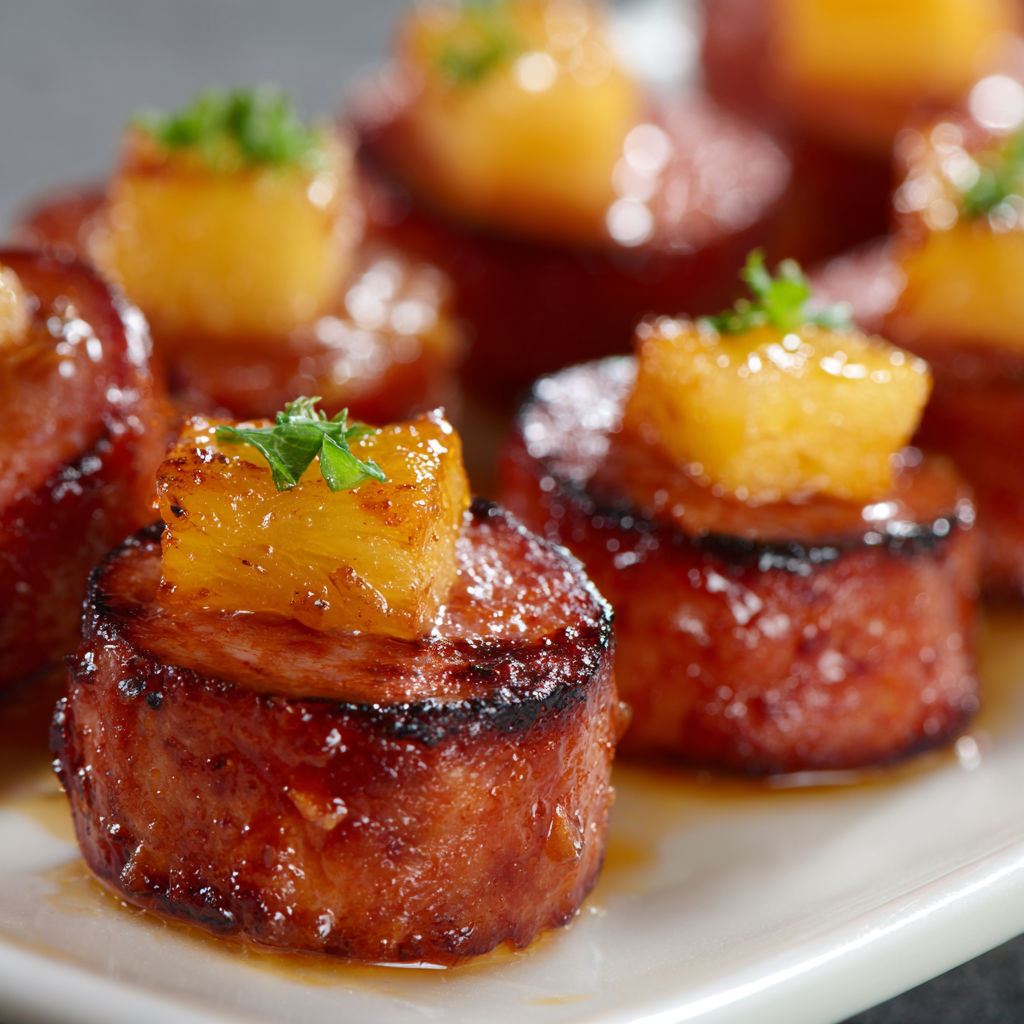 A plate of meat with pineapple on top.