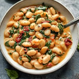 A hearty bean dish filling a bowl, garnished with green veggies and tomatoes.