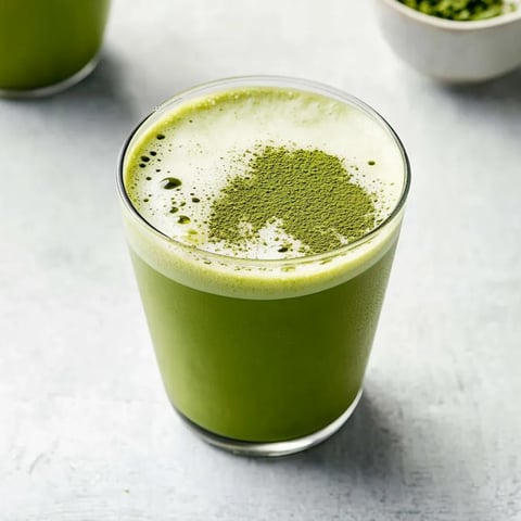 A cup of bright green tea with fresh leaves floating.