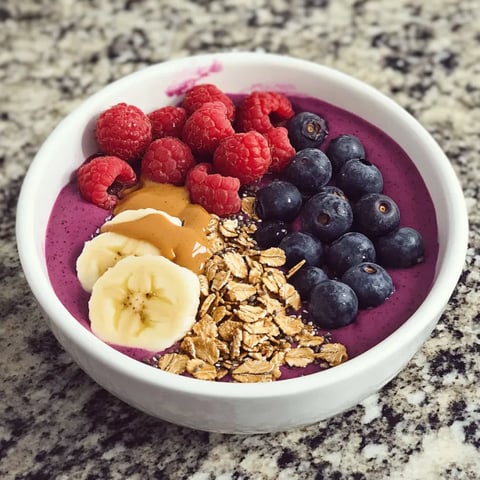 A bowl of fruit with bananas, raspberries, blueberries, and granola.