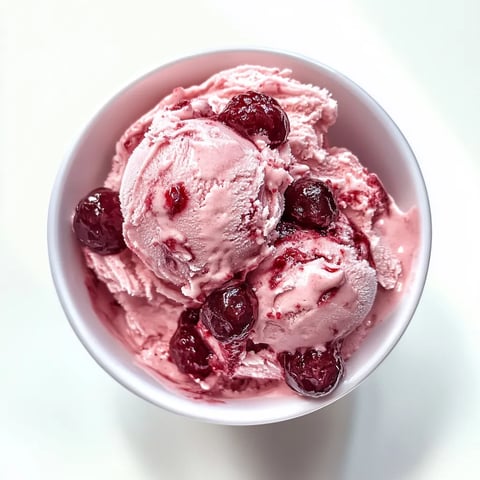 A bowl of pink ice cream with cherries on top.