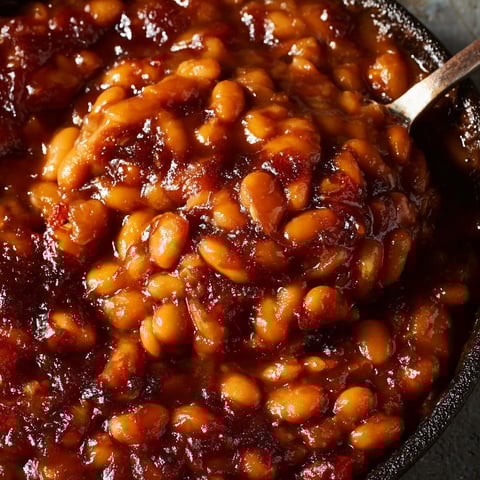 A bowl of baked beans with a spoon in it.