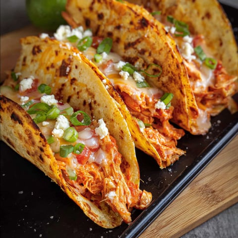 Three buffalo chicken tacos on a black cutting board.